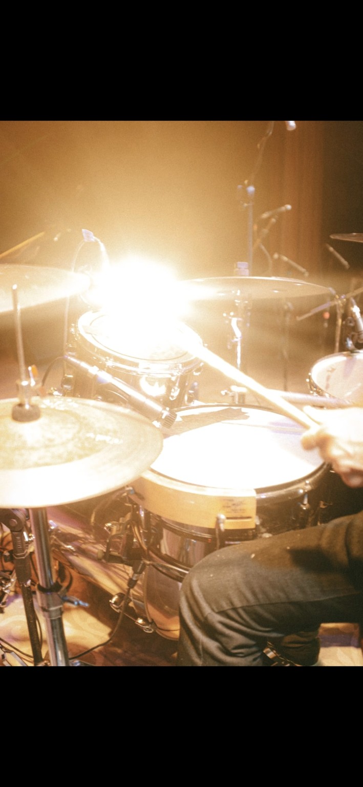 Detalhe de Rick de La Torre tocando bateria sob a luz do palco